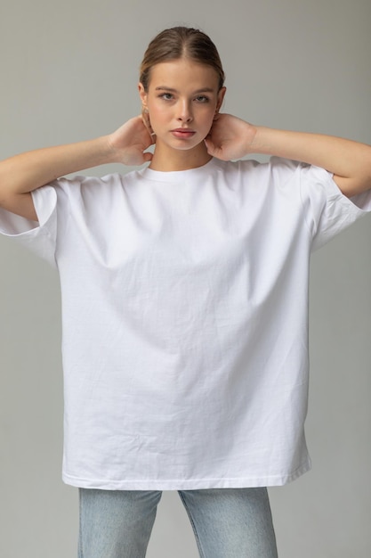 Beautiful blonde girl in a white oversized tshirt and blue jeans posing on a gray background