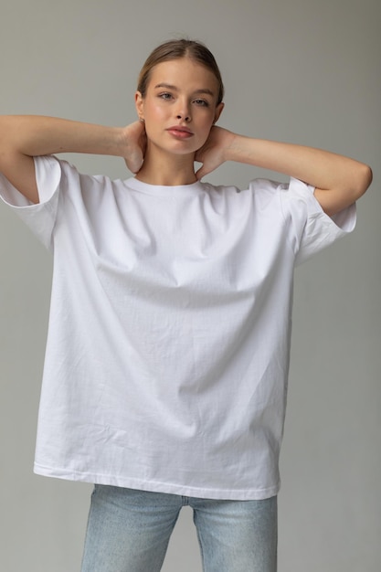 Free photo beautiful blonde girl in a white oversized tshirt and blue jeans posing on a gray background