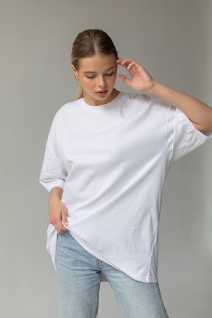 Beautiful blonde girl in a white oversized tshirt and blue jeans posing on a gray background