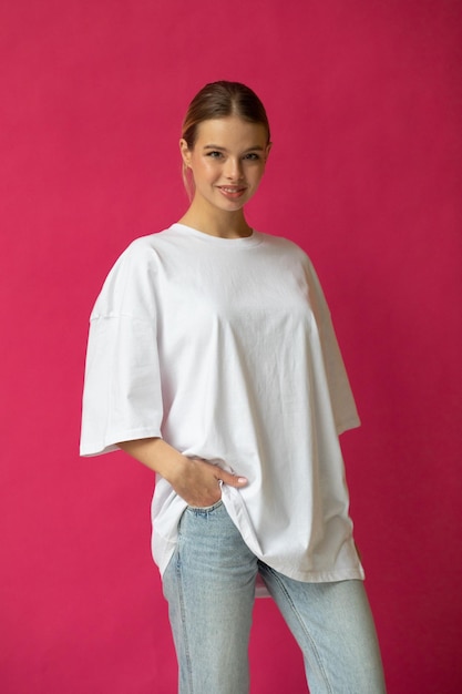 Beautiful blonde girl in a white oversized tshirt and blue jeans posing on a gray background