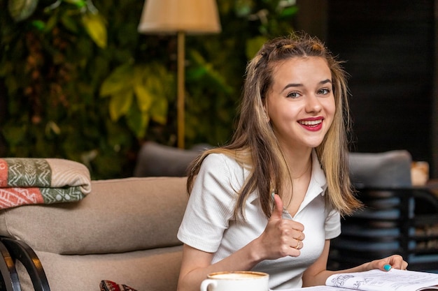 Free photo beautiful blonde sitting at the restaurant and gesture thump up