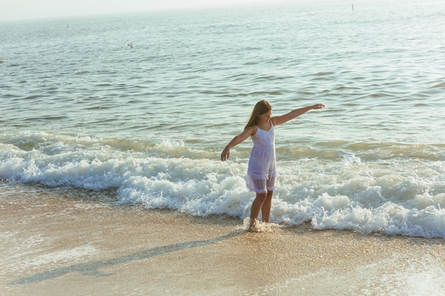 Beautiful blonde teenage girl wearing flowy white dress standing ankle dee in ocean water