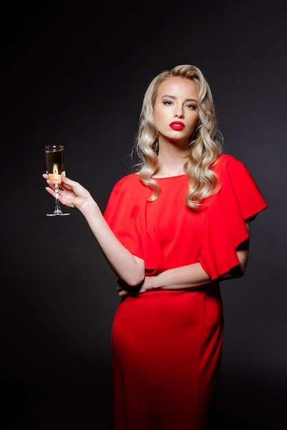 Красивая блондинка в вечернем платье позирует, держа шампанское стекло
