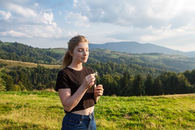 Beautiful blonde woman holding camomiles, carpathian mountains background