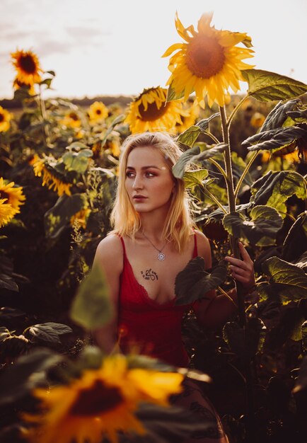 Beautiful blonde woman in a red dress in the field of sunflowers