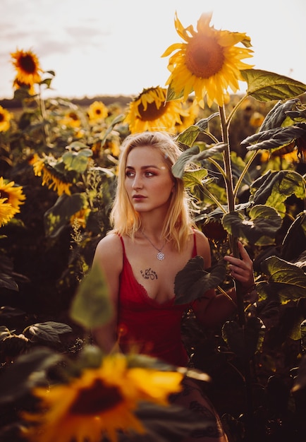 Beautiful blonde woman in a red dress in the field of sunflowers
