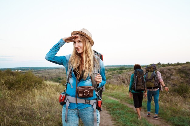 Beautiful blonde woman smiling, looking into distance, friends tourists background