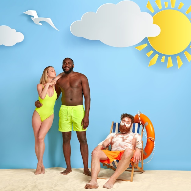 Free photo beautiful blonde woman stands with boyfriend near redhead posing at the beach with sunscreen