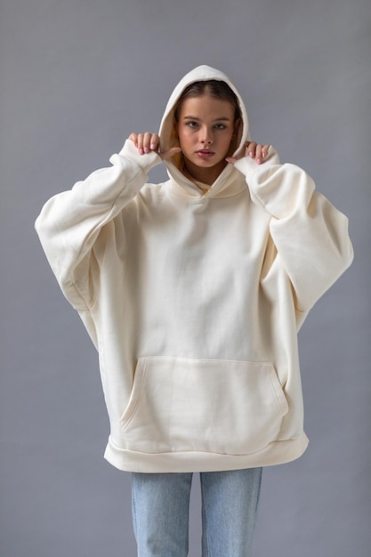 Beautiful blonde woman in a white hoodie and blue jeans posing on a gray background