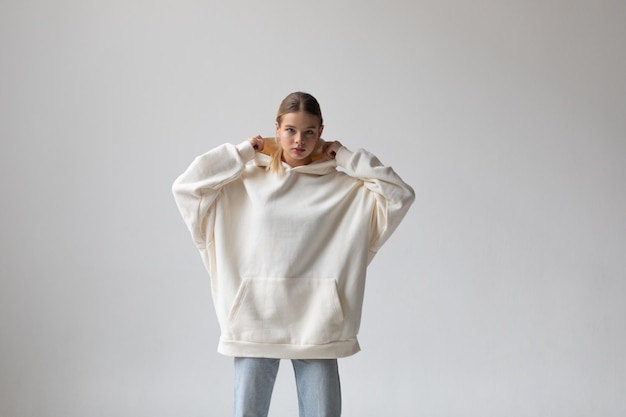 Beautiful blonde woman in a white hoodie and blue jeans posing on a white background