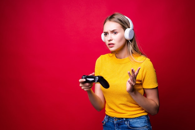 Foto gratuita bella donna bionda con joystick e cuffie sulla parete rossa