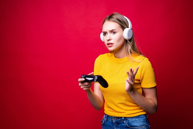 Beautiful blonde woman with joystick and headphones on red wall