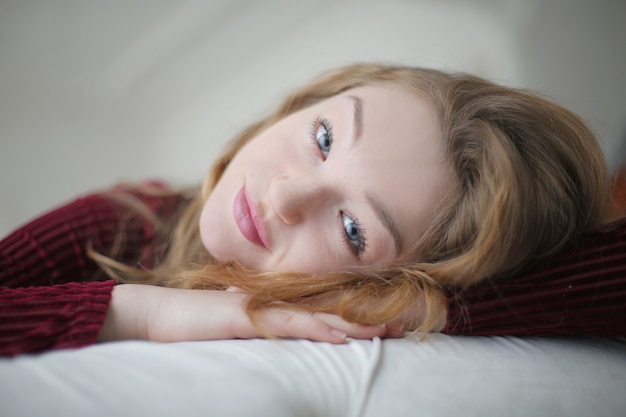 Beautiful blonde young female staring at the camera while lying on the bed