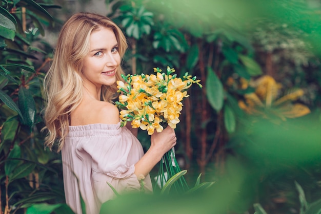 黄色のフリージアを保持している植物の近くに立っている美しい金髪の若い女性