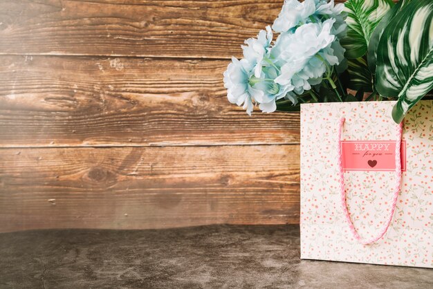 Beautiful blue artificial flowers in the paper bag against wooden backdrop