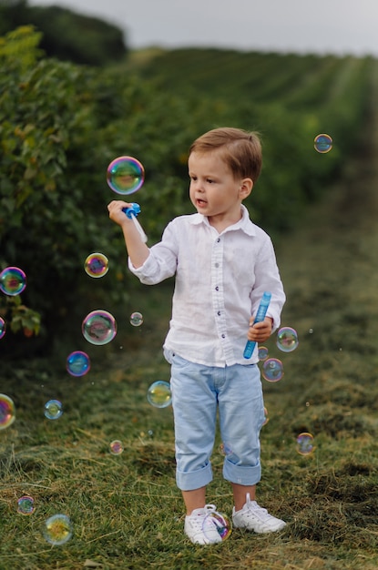 Красивый мальчик, играя с пузырьками в Солнечный день в саду.