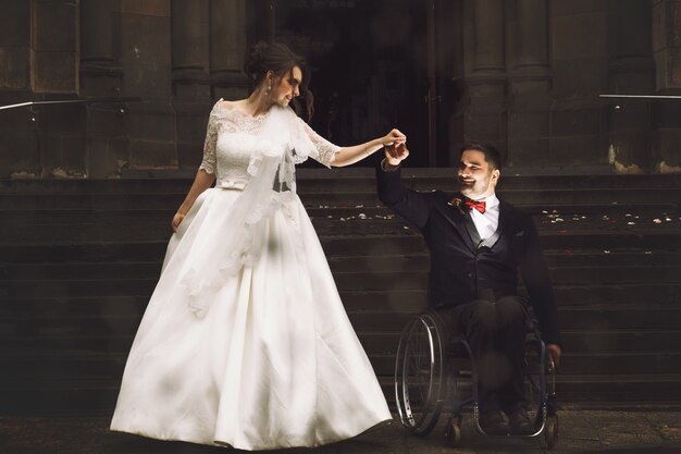 Beautiful bride and groom on the wheelchair dance before old Catholic church