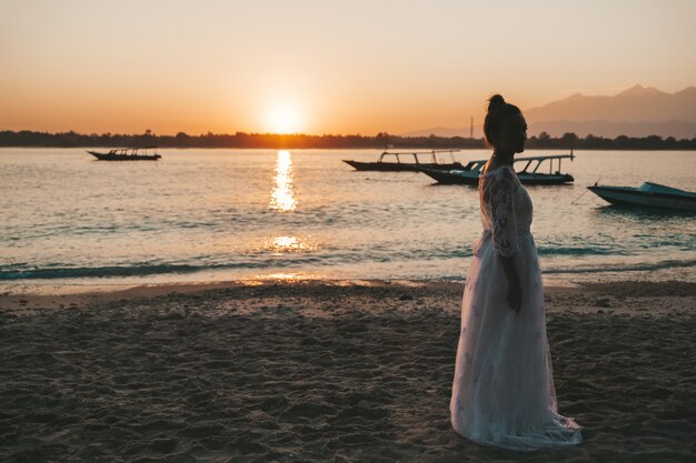 夕暮れ時、海の後ろのビーチでポーズ美しい花嫁
