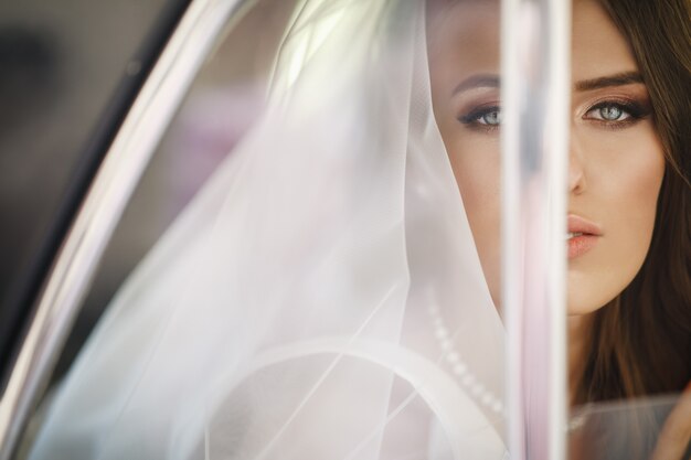 Beautiful bride sits with wedding bouquet in a retro car and has fun