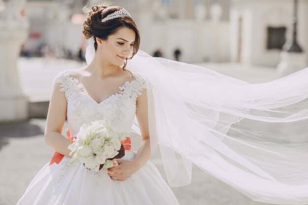 beautiful bride in a white dress and a crown on his head in a park and holding bouquet