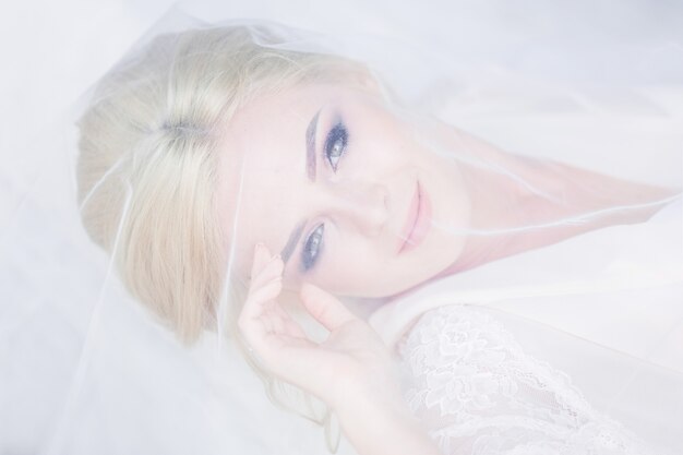 Красивая невеста в белом белье лежит на кровати, скрытой под вуалью