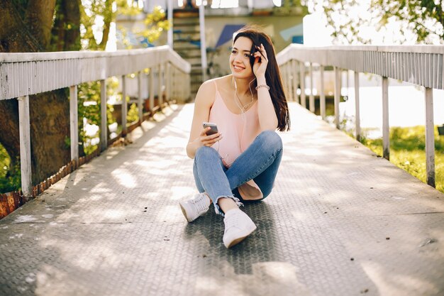 beautiful and bright girl in pink t-shirts and blue jeans sitting in the sunny summer park