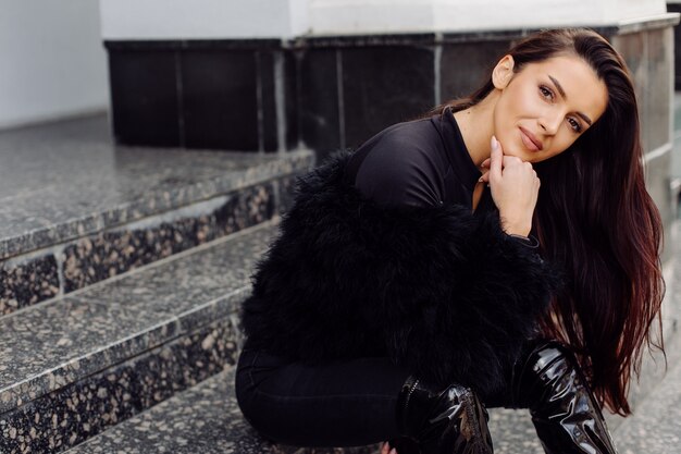 Beautiful brown-haired stylish girl in black dress outdoor. Young attractive elegant woman portrait with long hair on springtime in city streets.