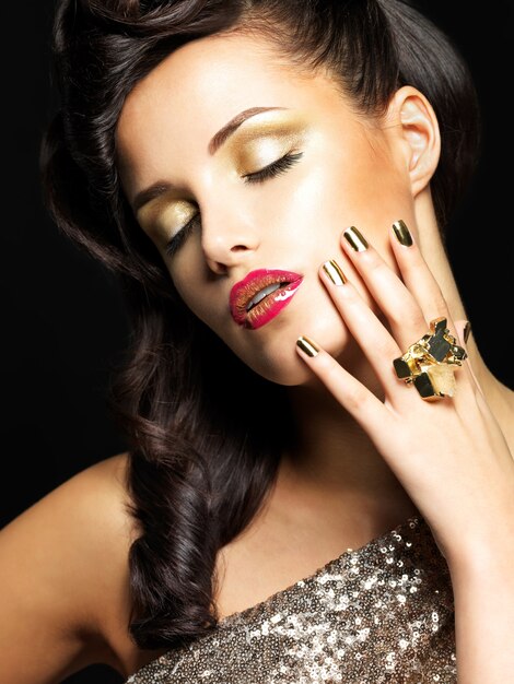 Beautiful brunet woman with golden nails and style makeup of eyes -  on black background