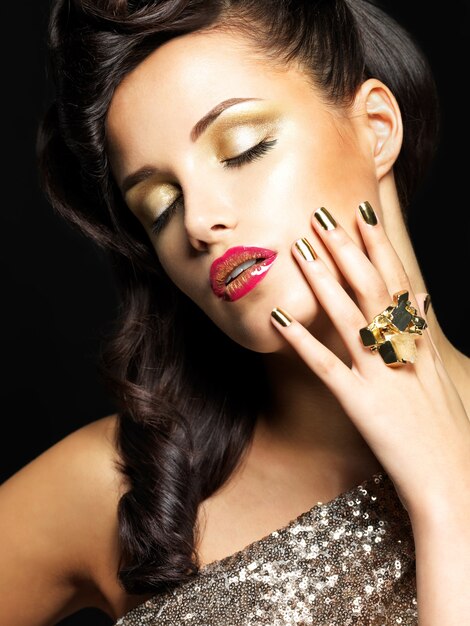 金色の爪と目のスタイルのメイクアップを持つ美しい黒髪の女性-黒い背景に