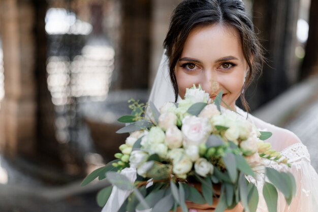 Beautiful brunette bride is looking straight and holding wedding bouquet near face