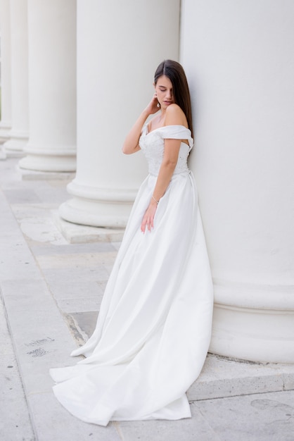 Красивая брюнетка невеста стоит возле огромной белой колонны