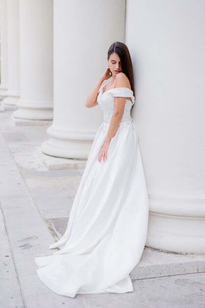 Beautiful brunette bride is standing near the huge white column