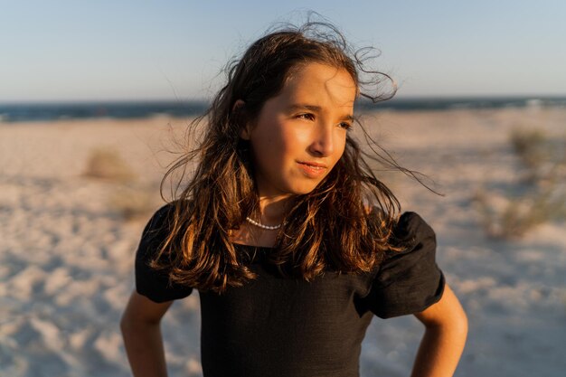 해변에서 포즈를 취하는 아름다운 갈색 머리 아이 소녀 일몰 따뜻한 색상