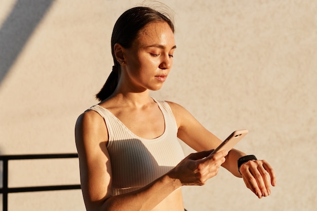 Foto gratuita bella donna bruna con coda di cavallo che indossa un top bianco, che collega il suo smartphone