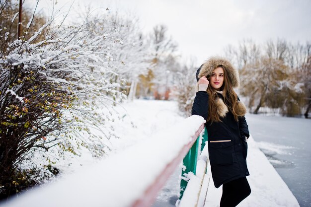 Beautiful brunette girl in winter warm clothing Model on winter jacket against frozen lake at park