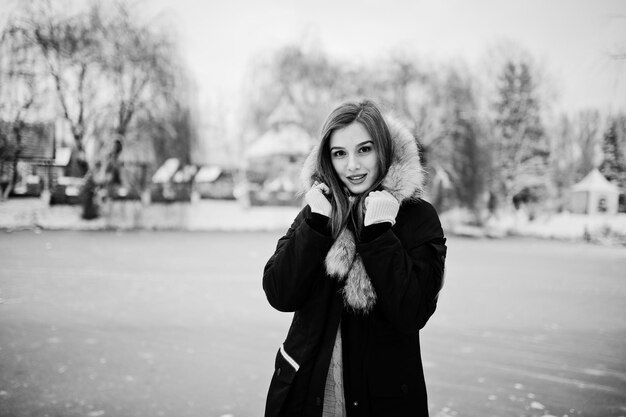 Beautiful brunette girl in winter warm clothing Model on winter jacket against frozen lake at park