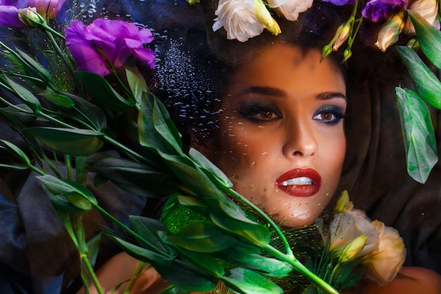 Beautiful brunette girl with bright make up lying among eustomas.