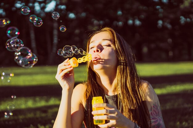 beautiful brunette girl with long hair puffs up soap bubbles in the park