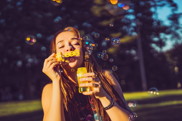 beautiful brunette girl with long hair puffs up soap bubbles in the park