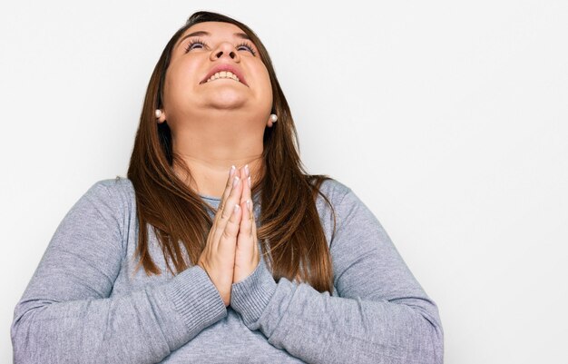 Beautiful brunette plus size woman wearing casual clothes begging and praying with hands together with hope expression on face very emotional and worried begging