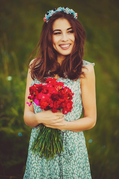 彼女の腕の中に赤い花を持つ美しいブルネット