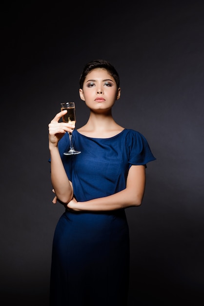 Красивая брюнетка женщина в вечернем платье позирует, держа шампанское стекло