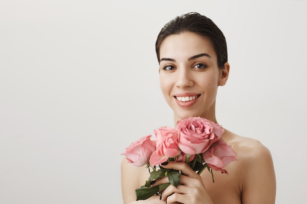 バラの花束と裸で立っている美しいブルネットの女性