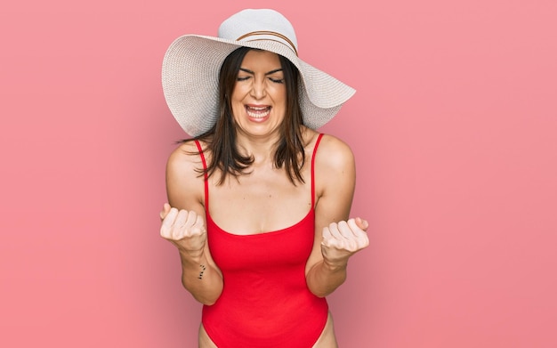 Free photo beautiful brunette woman wearing swimsuit and summer hat very happy and excited doing winner gesture with arms raised smiling and screaming for success celebration concept