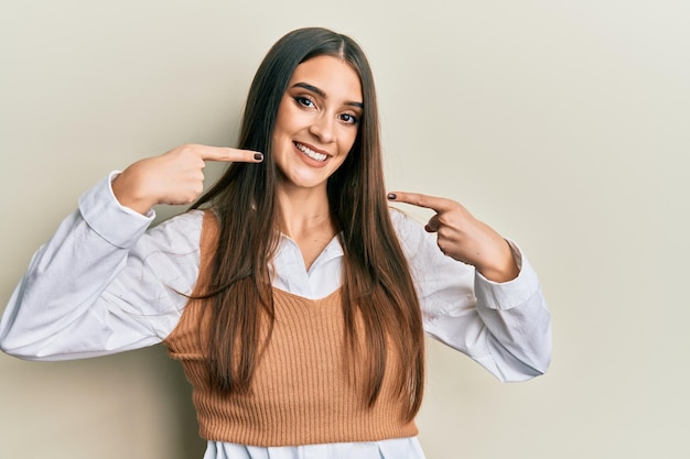 Beautiful brunette young woman wearing casual clothes smiling cheerful showing and pointing with fingers teeth and mouth. dental health concept.