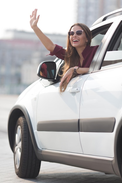 Bella donna d'affari agitando la mano e sorridendo seduta nella sua macchina costosa