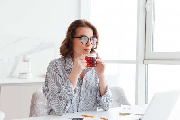 красивая деловая женщина в повседневной одежде, пить горячий чай, сидя и отдыхая после оформления документов на дому
