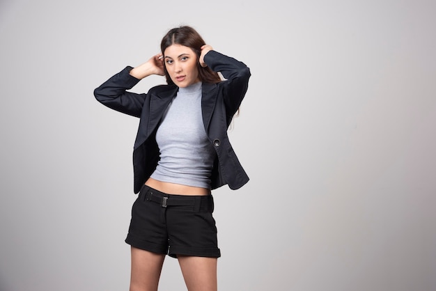 Beautiful businesswoman in jacket standing and posing over a gray wall. 