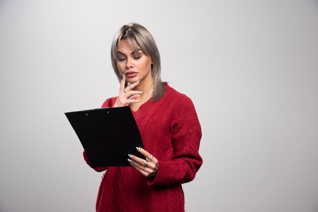 Beautiful businesswoman looking at clipboard on gray background.