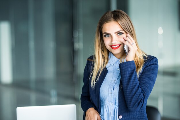 Beautiful Busy Businesswoman, standing in office, writing in planner and talking on mobile phone.